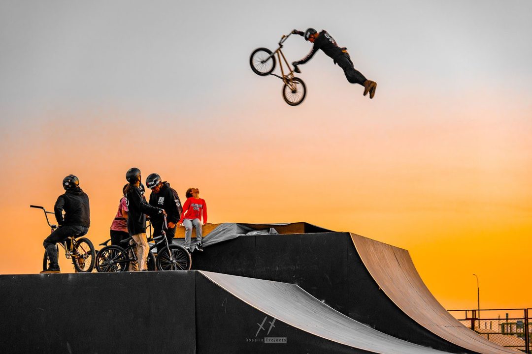 BMX Rider jumps high in the sky over a ramp with onlookers looking up from directly below.